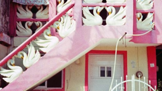 Picture of a two story barrio house painted in pink with decorative white swans